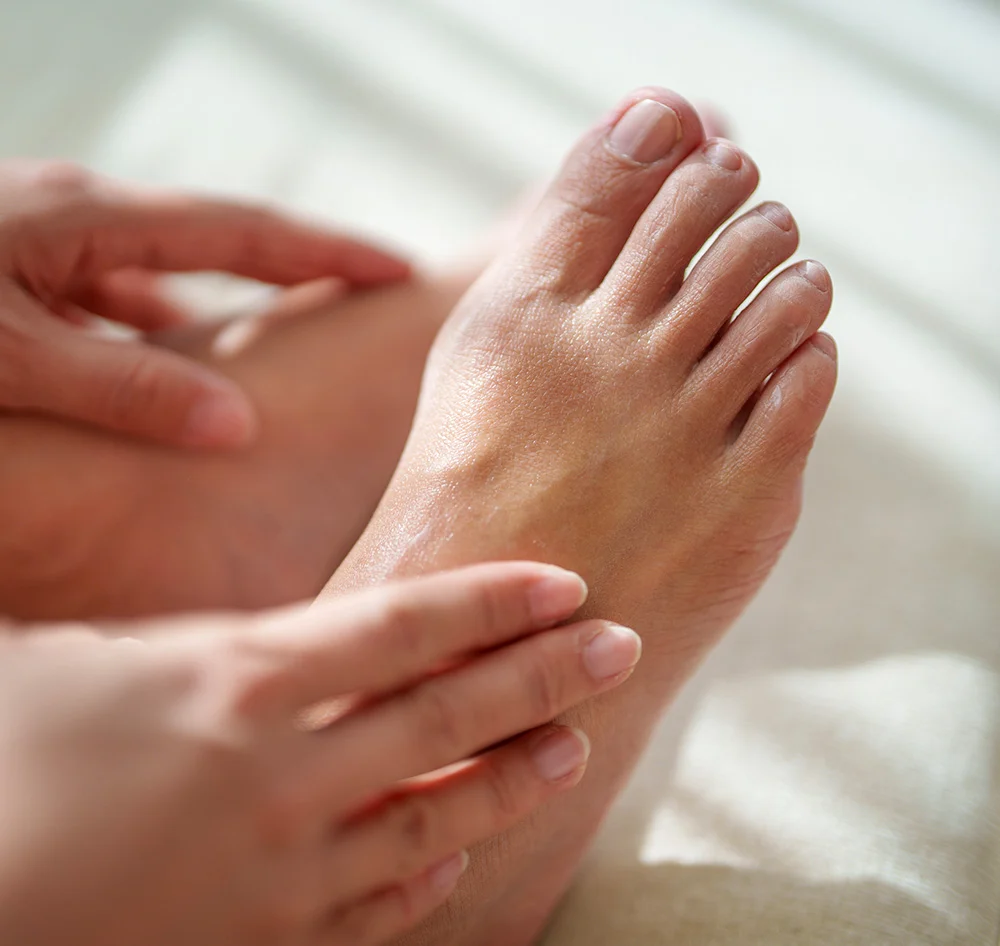 A close-up shot of a person's foot as it is being massaged by two hands. The hands are rubbing a substance into the skin on the top of the foot. - onychomycosis in Queensbury, NY