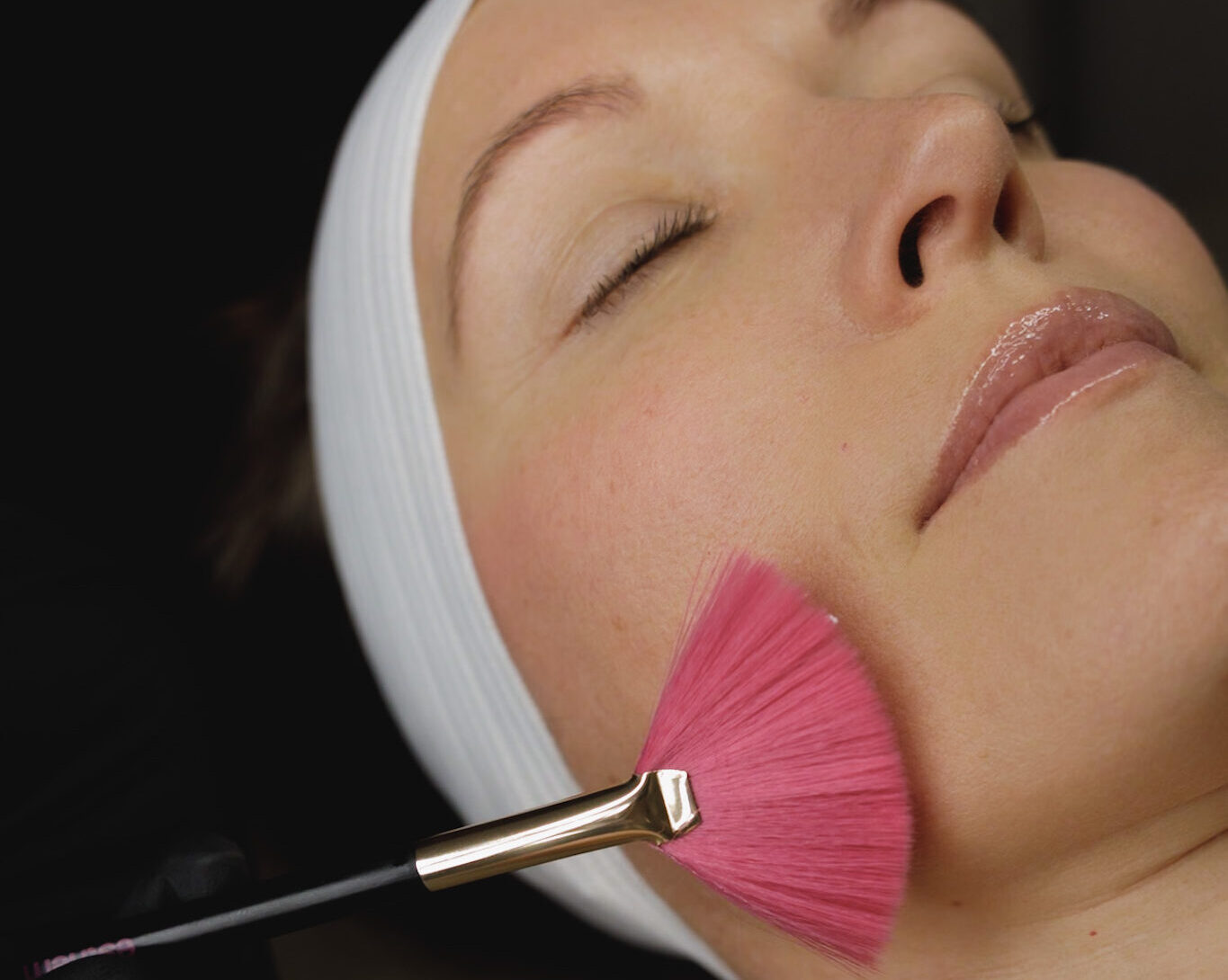 close up of woman laying down with pink brush being applied to her face. Chemical peels in Queensbury New York