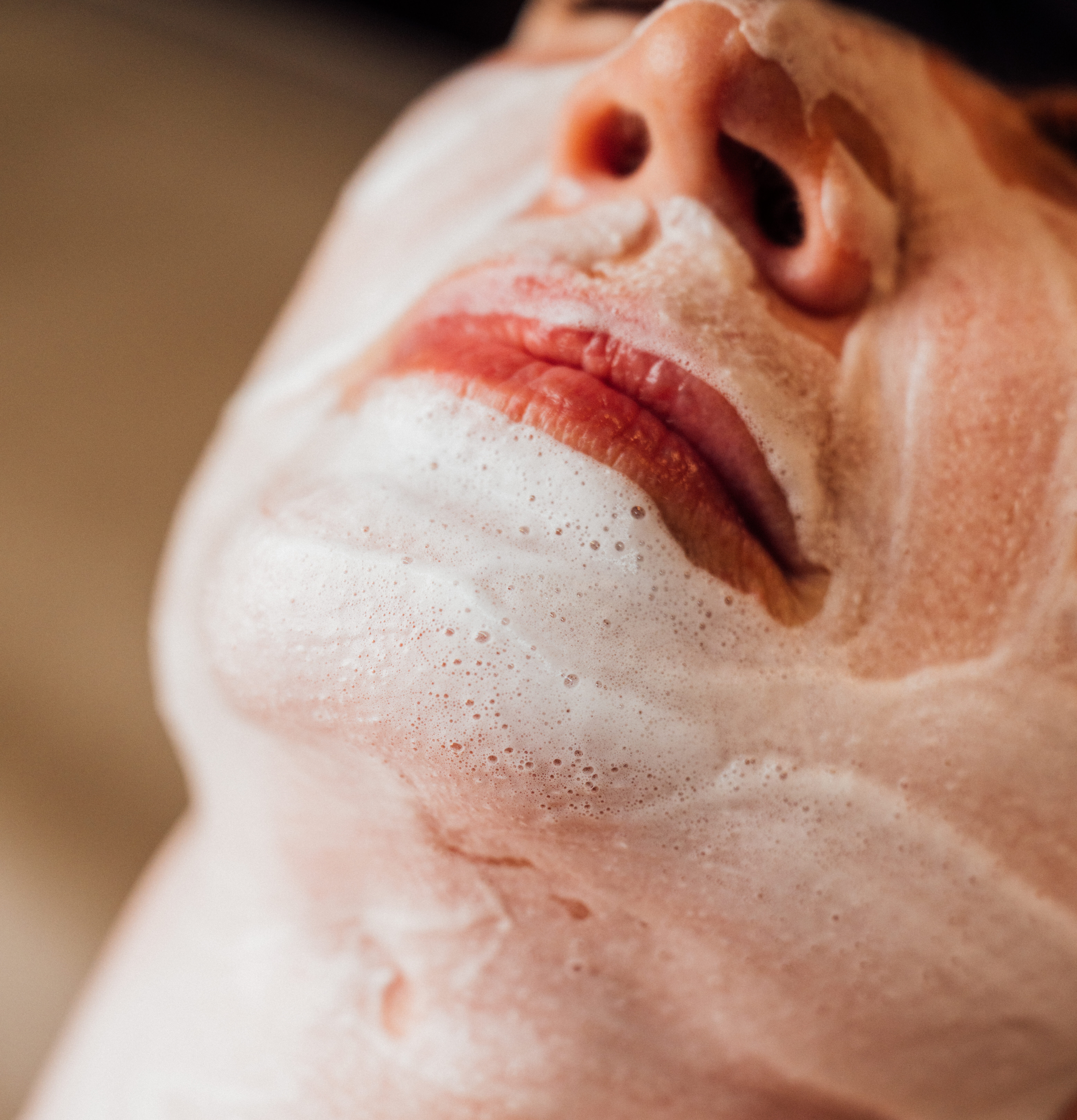 A close-up of a womans face lying down getting a facial- white cleanser on face. Facials in Queensbury, NY
