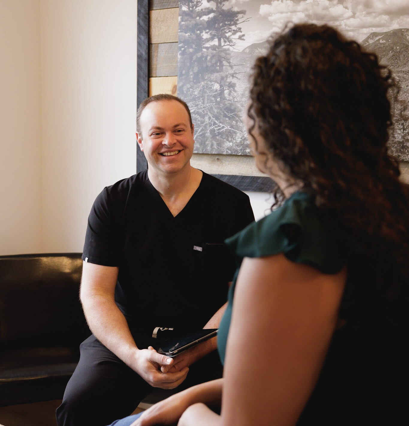 Dr. Gregory Sheehan smiling and talking with a patient while holding an ipad in an exam room at Elevation Medical Aesthetics