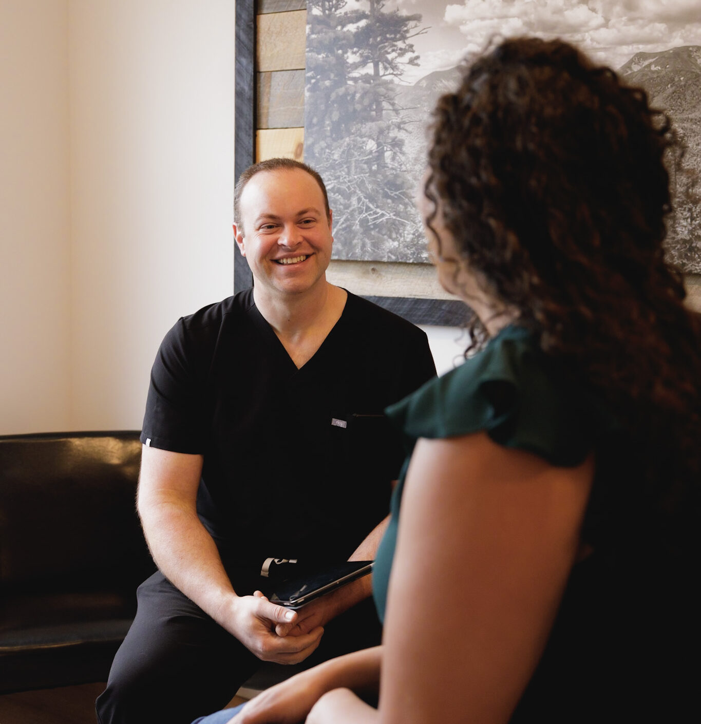 Dr. Gregory Sheehan, Medical Director and Co Founder of Elevation Medical Aesthetics smiling and talking with a female patient in an exam room