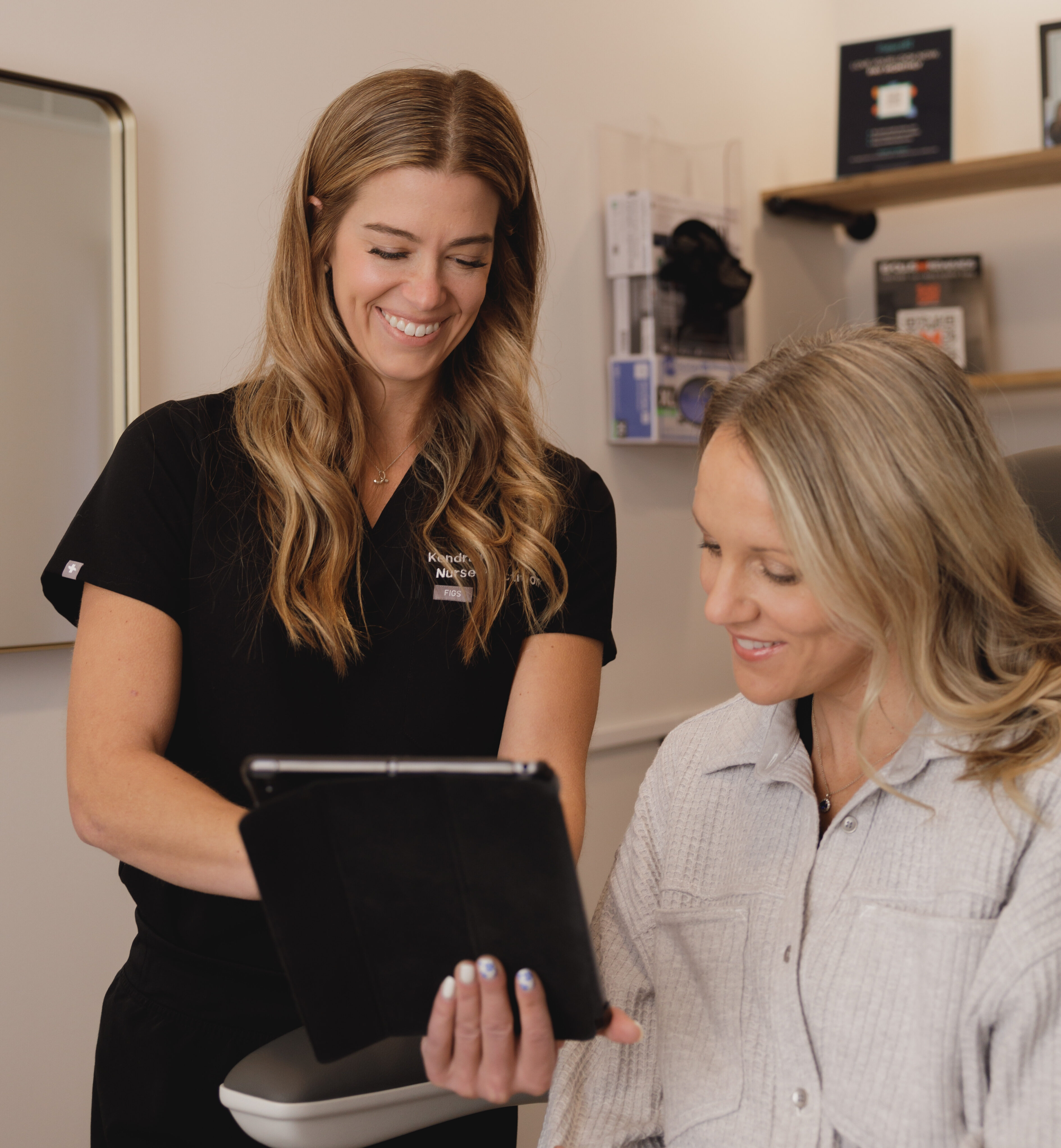 Aesthetic Nurse Practitioner Kendra Kline showing a female patient her results pointing on a black ipad. Kendall and the patient are smiling at Elevation Medical Aesthetics